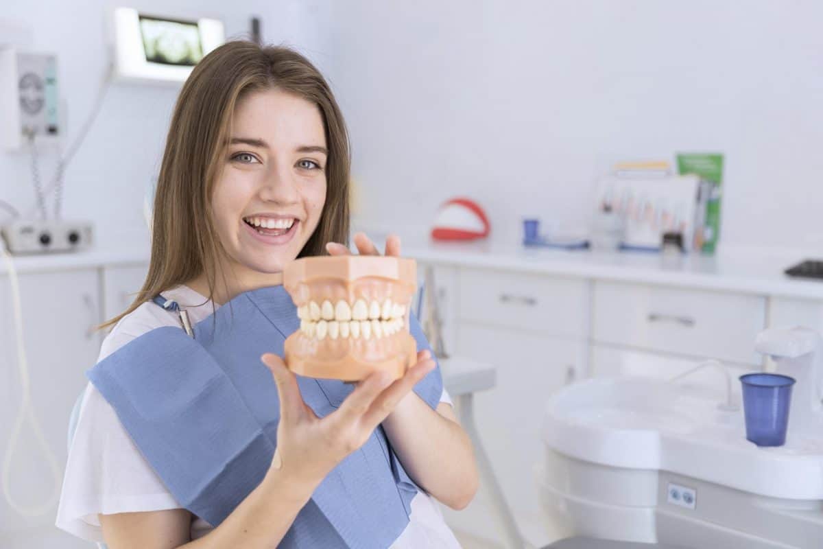 smiling-young-woman-holding-denture-in-her-hands-at-dental-clinic-1200x800.jpg